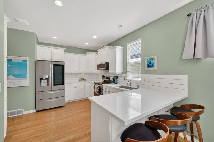 Kitchen featuring a kitchen breakfast bar, stainless steel appliances, white cabinets, a peninsula, and backsplash