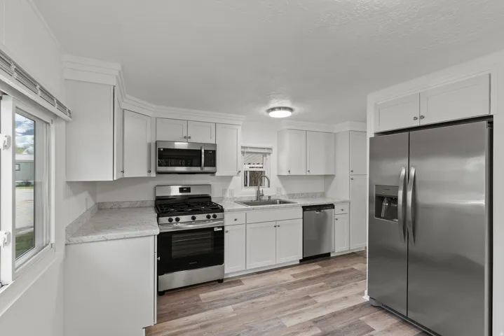 Kitchen with stainless steel appliances, light countertops, white cabinets, light wood finished floors, and a textured ceiling