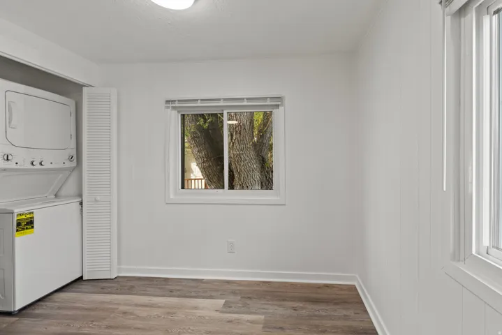 Laundry area with stacked washer and clothes dryer and wood finished floors