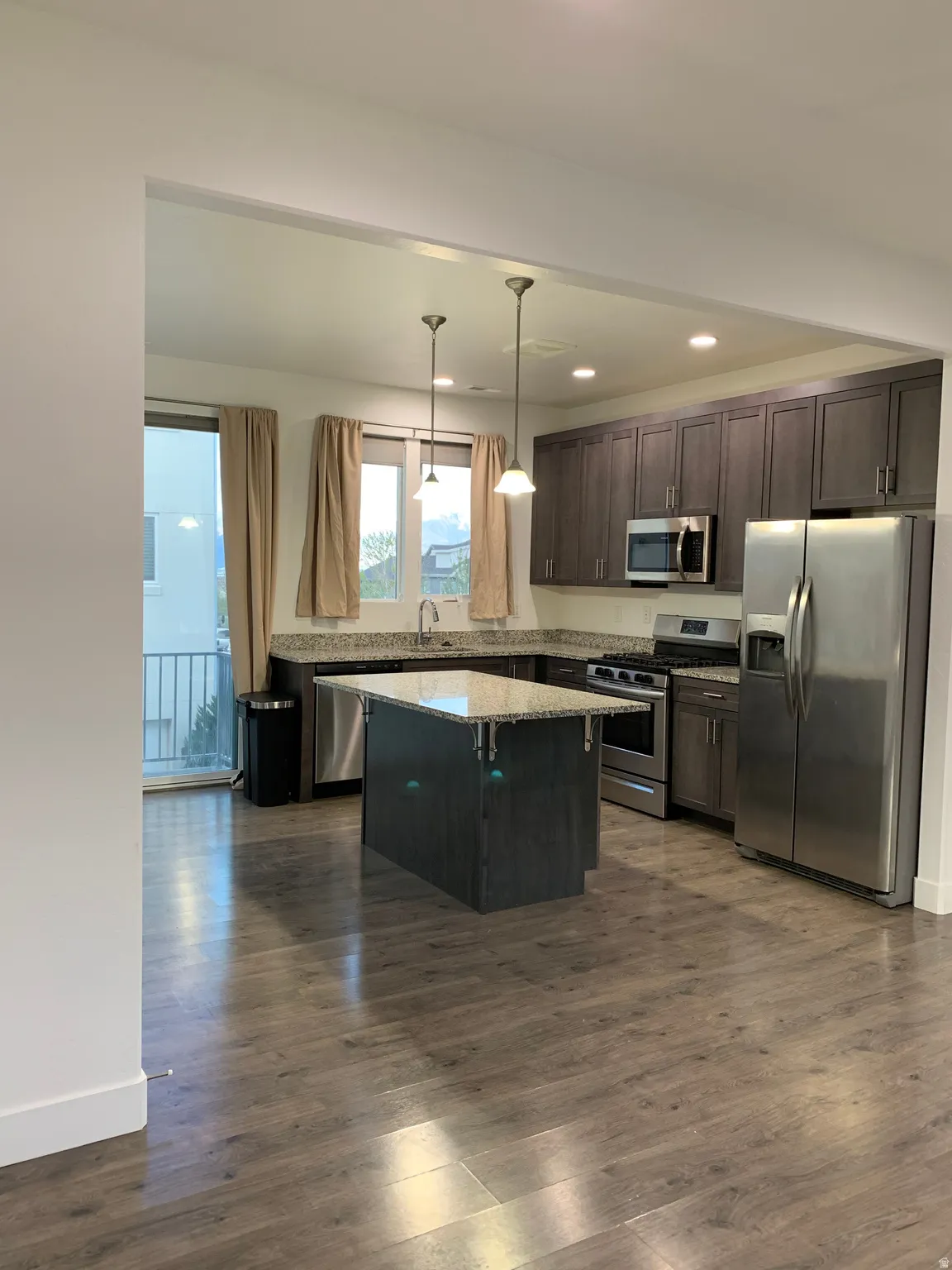 Kitchen featuring cabinets, stainless steel appliances, granite countertops, pendant lighting, and wood-like finished floors
