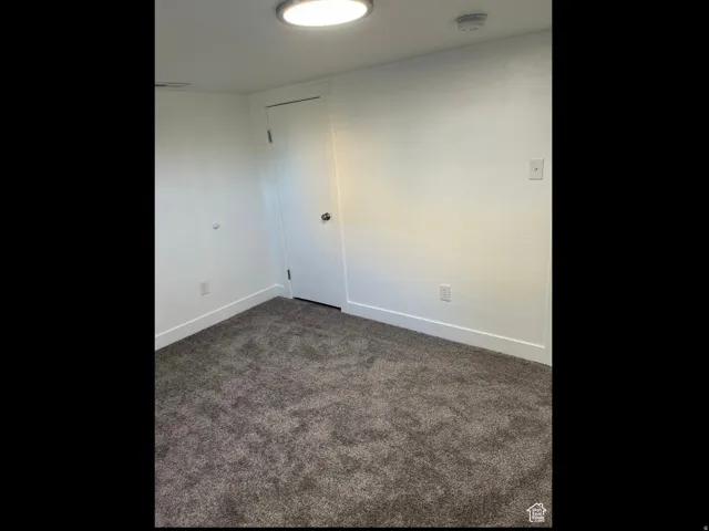 Empty room featuring dark carpet and a smoke detector