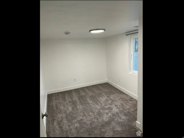 Unfurnished room featuring dark carpet and baseboards
