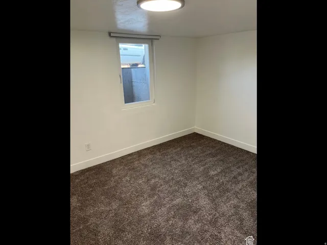 Spare room featuring dark carpet and baseboards