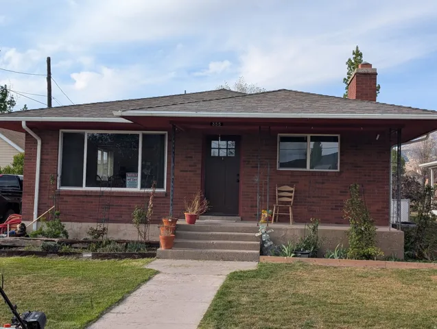 View of front of property with a front lawn, a chimney, brick siding, and roof with shingles