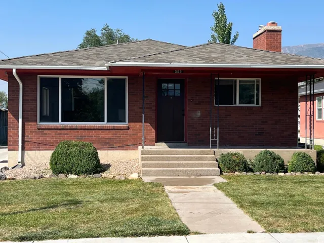 View of front of house with a front yard, a shingled roof, a chimney, and brick siding