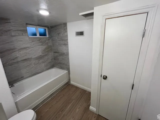 Bathroom with dark wood-style flooring, a textured ceiling, and tub / shower combination
