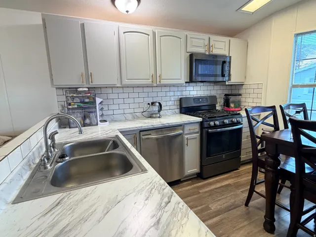 Kitchen featuring a stainless steel double sink, white marble-look countertops, white subway tile backsplash, and light gray cabinetry