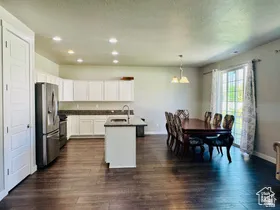 Kitchen featuring white cabinets, stainless steel appliances, a center island with sink, dark wood finished floors, and dark countertops