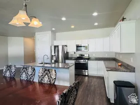 Kitchen with stainless steel appliances, decorative light fixtures, a center island with sink, white cabinetry, and dark wood-type flooring