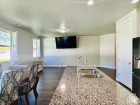 Kitchen with light stone countertops, dark wood-style flooring, black fridge with ice dispenser, a kitchen island with sink, and a textured ceiling