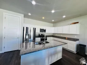 Kitchen featuring stainless steel appliances, a kitchen island with sink, white cabinets, dark stone counters, and dark wood finished floors