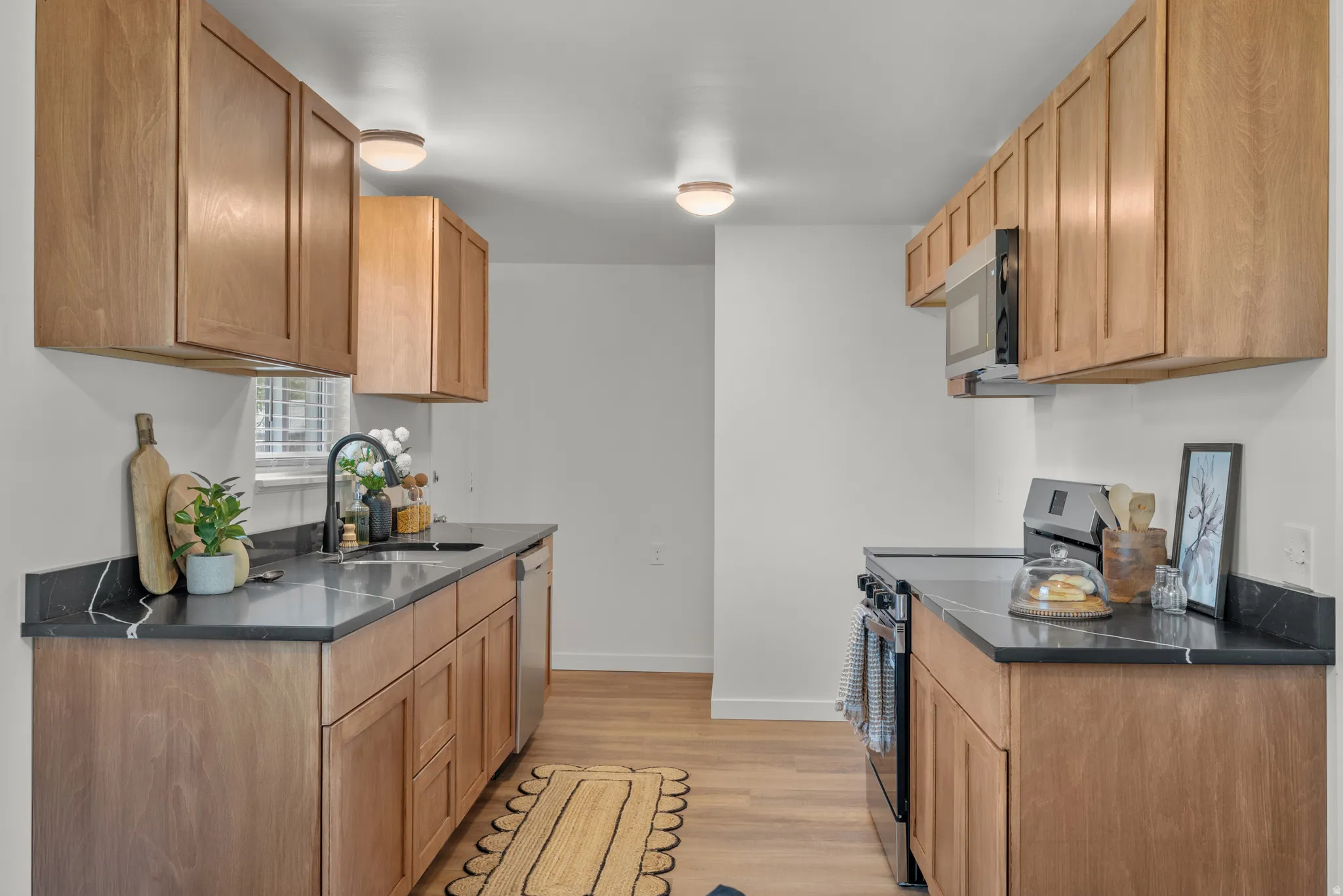 Kitchen with stainless steel appliances, light wood finished floors, and dark stone countertops