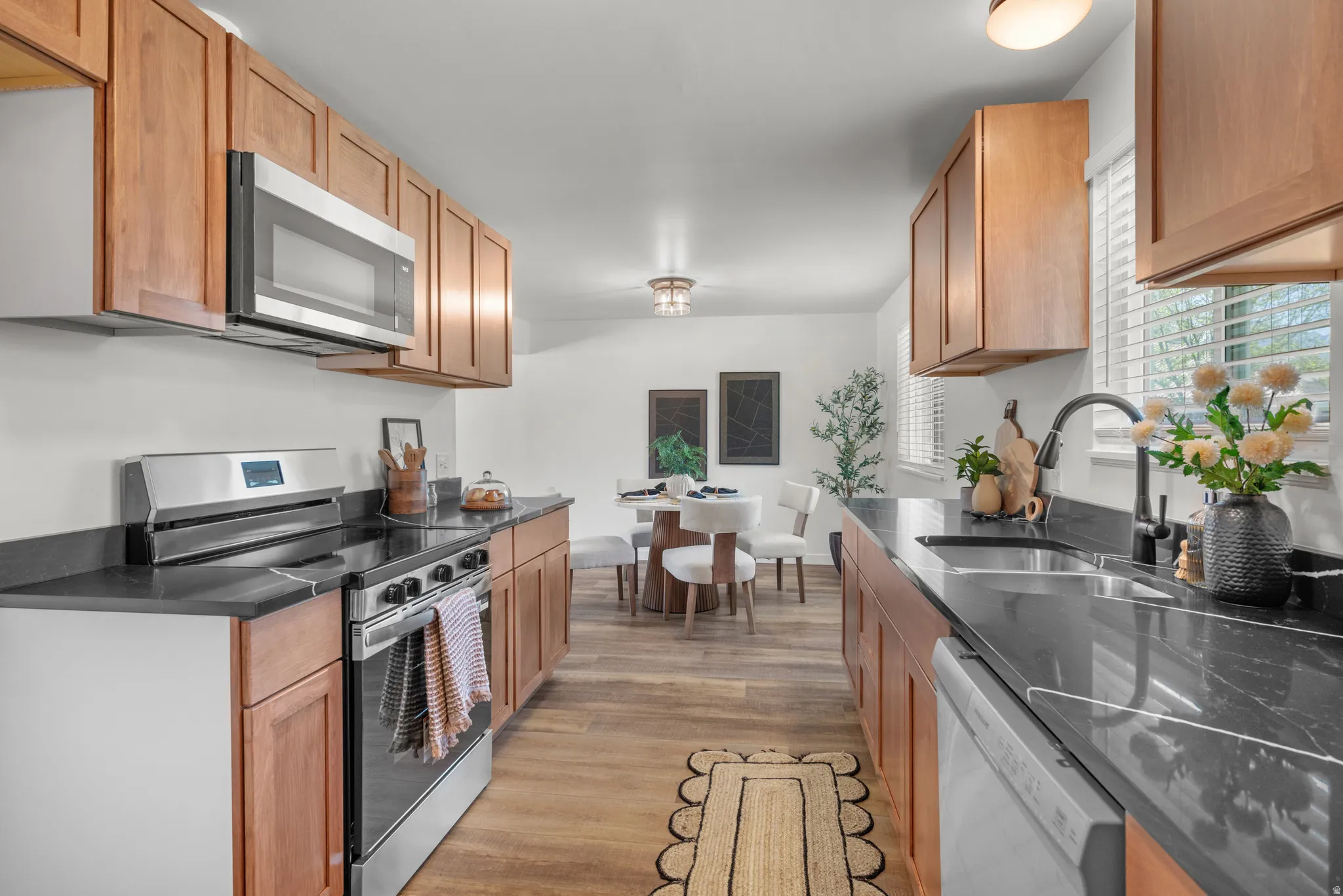 Kitchen featuring stainless steel appliances, light wood-type flooring, dark stone counters, and wood finish cabinets