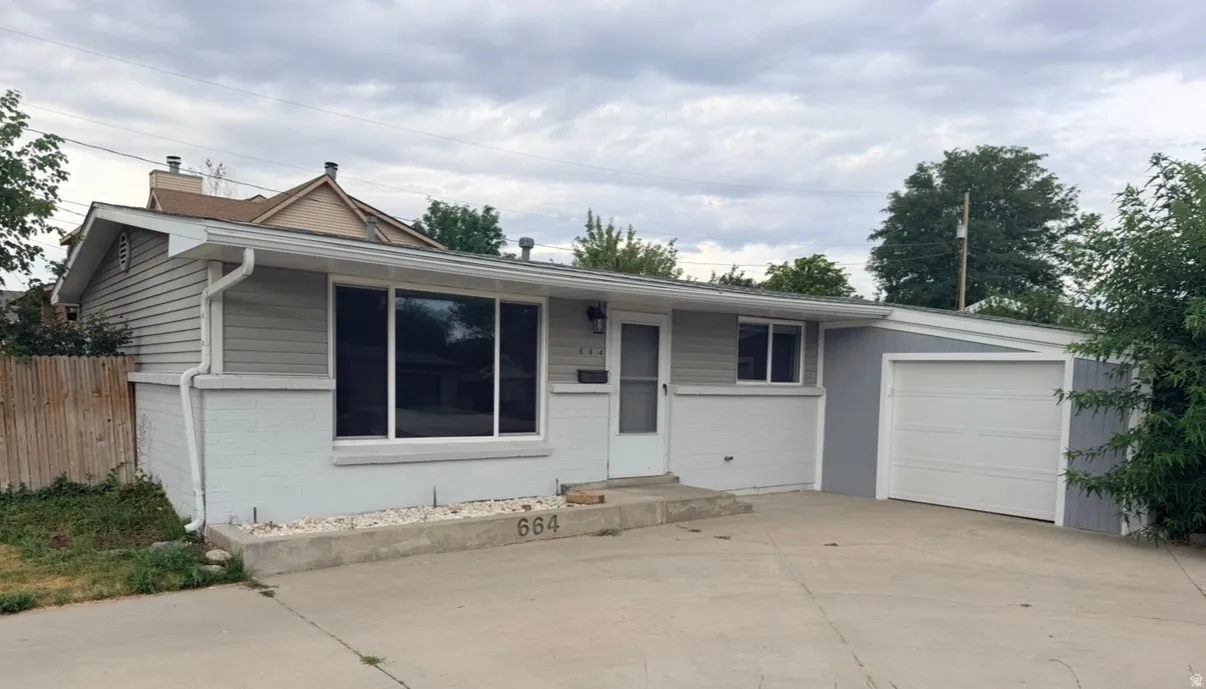 Single-story residence featuring light gray siding with white trim, a sloped roofline, attached garage with white door, and a concrete driveway