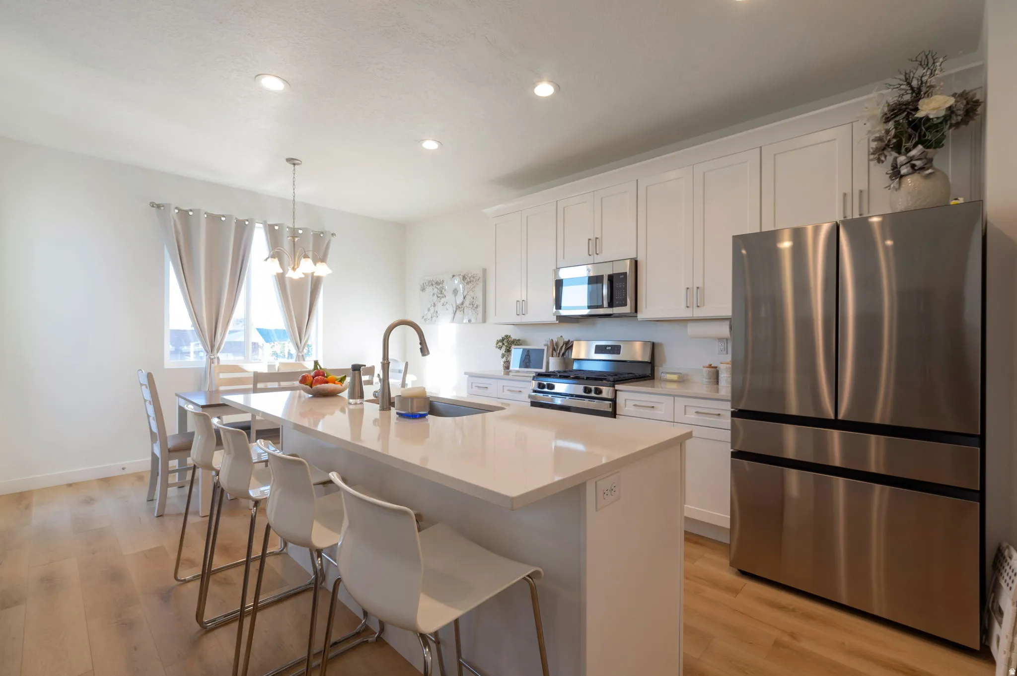 Kitchen with stainless steel appliances, white cabinets, a center island with sink, a kitchen breakfast bar, and light wood finished floors
