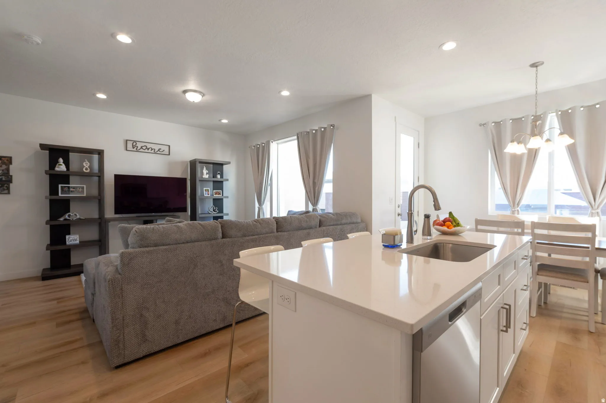 Kitchen featuring light wood-type flooring, open floor plan, an island with sink, white cabinetry, and dishwasher