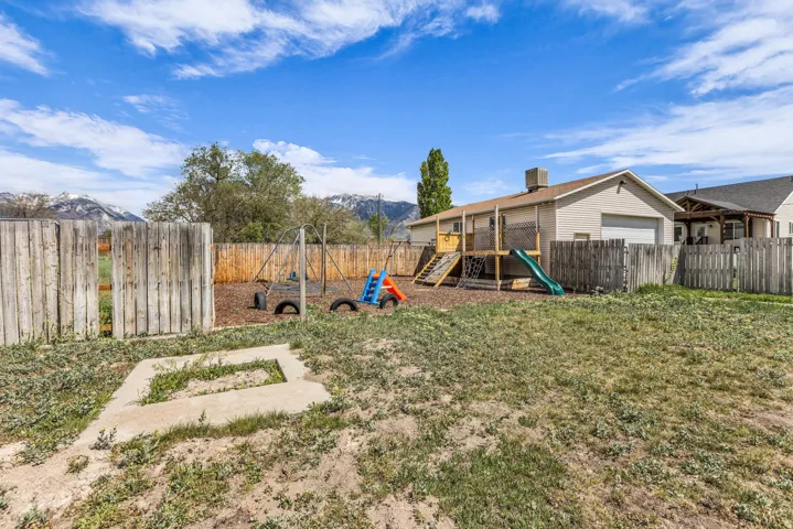 Fenced backyard featuring a playground, a mountain view, and a garage