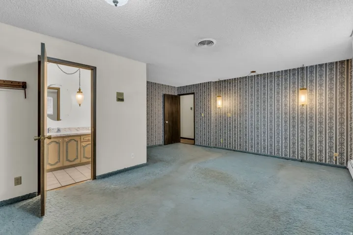 Empty room featuring light colored carpet, a textured ceiling, and wallpapered walls