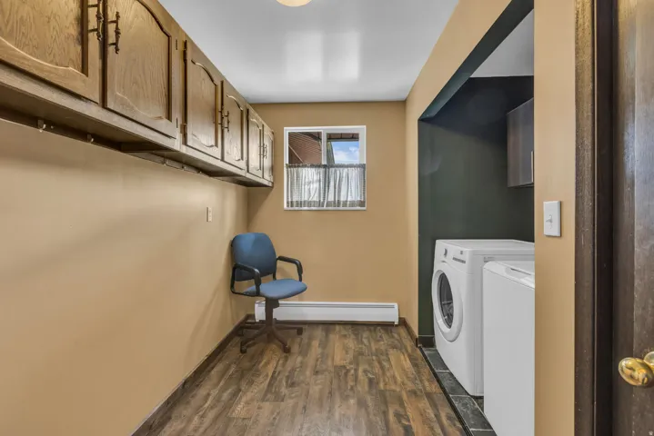 Laundry room with dark wood-style floors, baseboard heating, cabinet space, and washer and dryer
