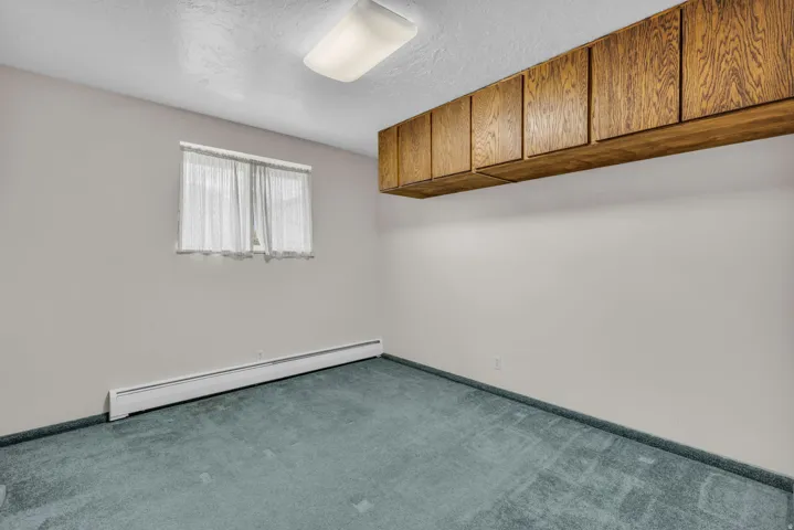 Carpeted spare room featuring a baseboard heating unit and a textured ceiling