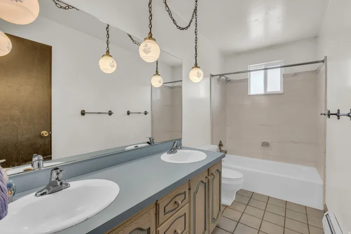 Bathroom with double vanity, light tile patterned floors, tub / shower combination, and a baseboard radiator