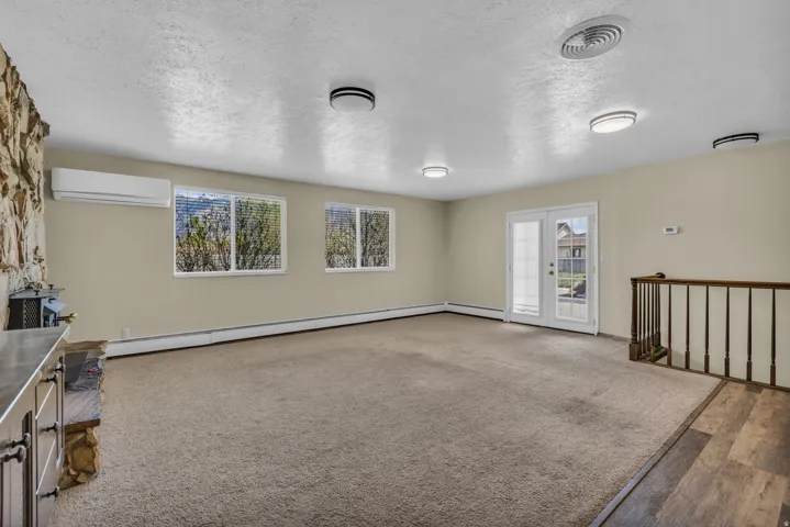 Unfurnished living room with a textured ceiling, french doors, healthy amount of natural light, a baseboard heating unit, and carpet