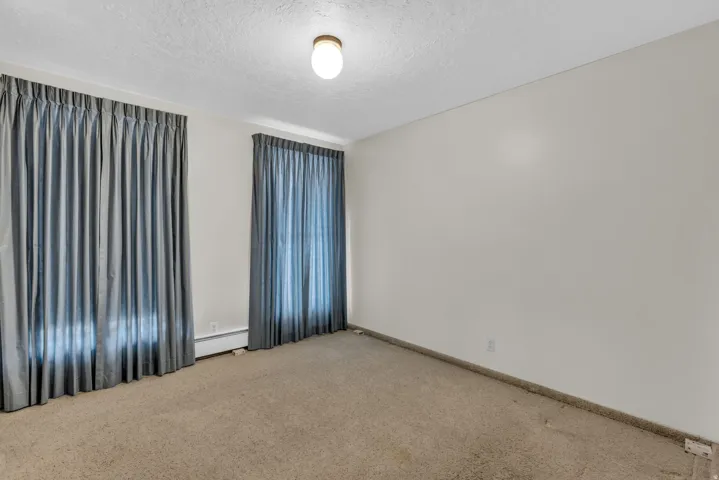 Unfurnished room with a textured ceiling, light colored carpet, and a baseboard radiator