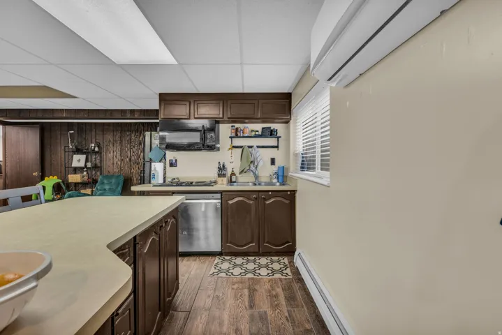 Kitchen with dark wood finish cabinetry, a baseboard heating unit, light countertops, a drop ceiling, and dark wood-style floors
