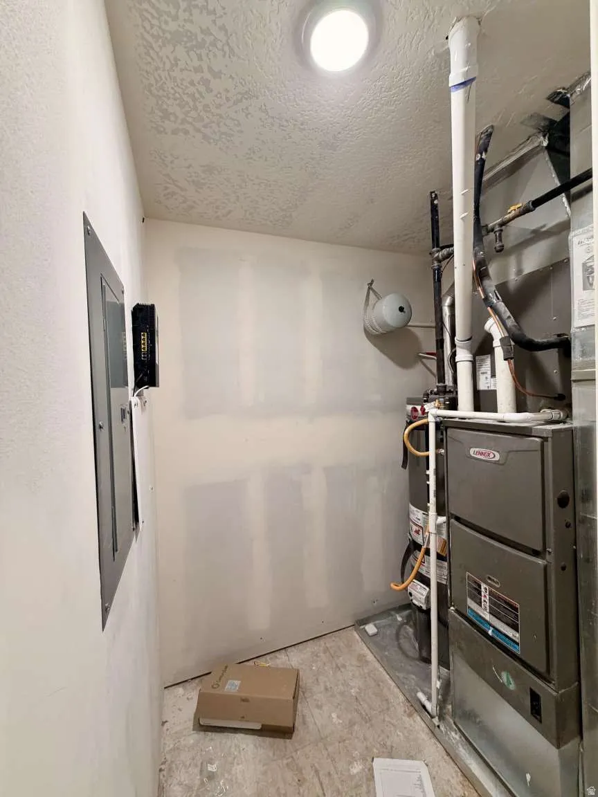 Utility room featuring a Lennox furnace, water heater, electrical panel, recessed ceiling light, and textured ceiling finish