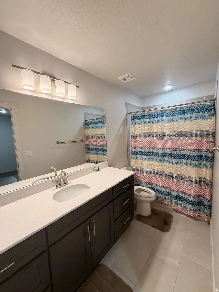 Single vanity featuring a white oval sink set in a light-toned countertop, dark wood-finish cabinetry with brushed nickel pulls, and a large wall-mounted mirror
