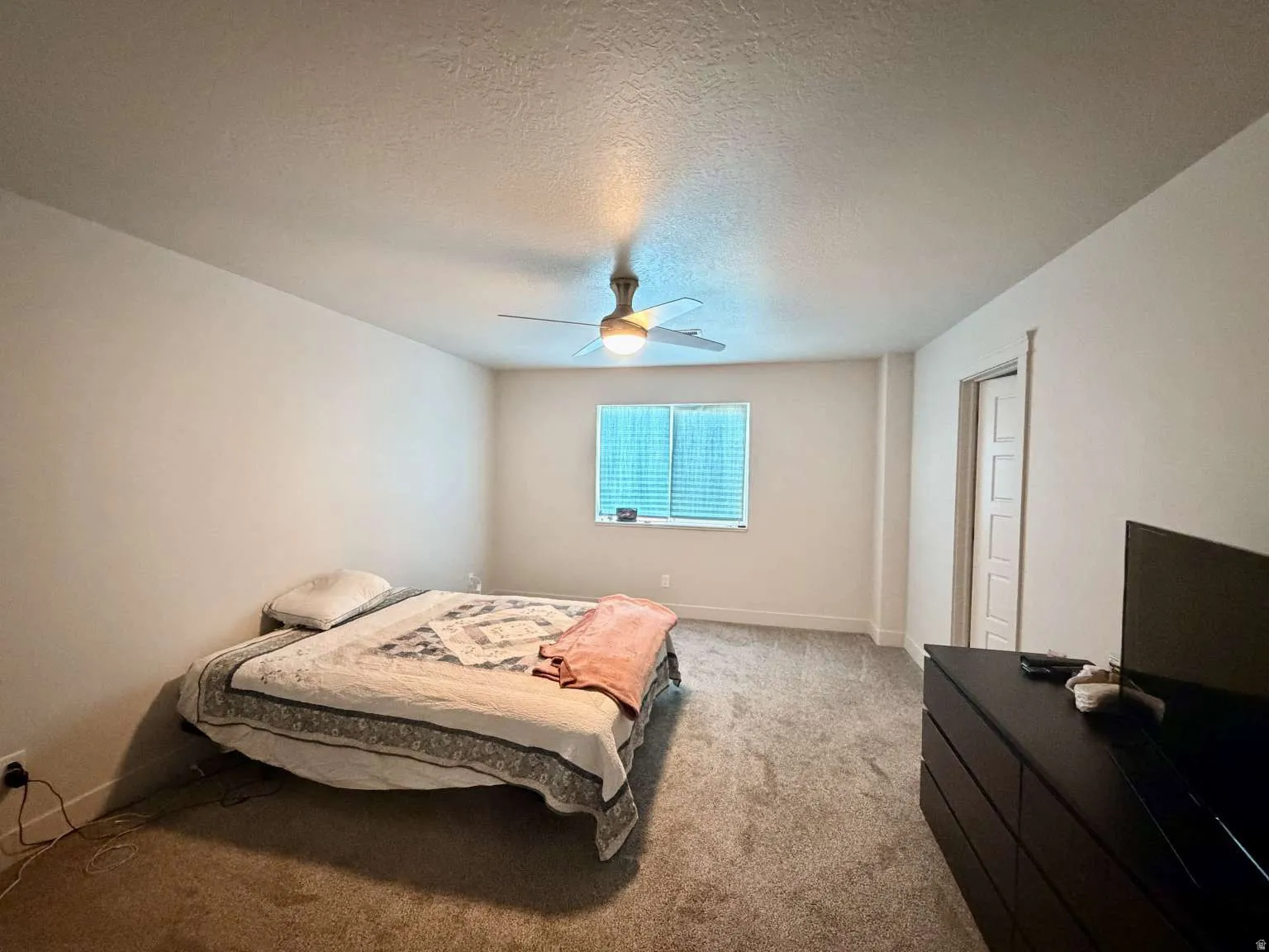 Bedroom featuring neutral-toned walls, textured ceiling, a ceiling fan with integrated lighting, and carpet flooring