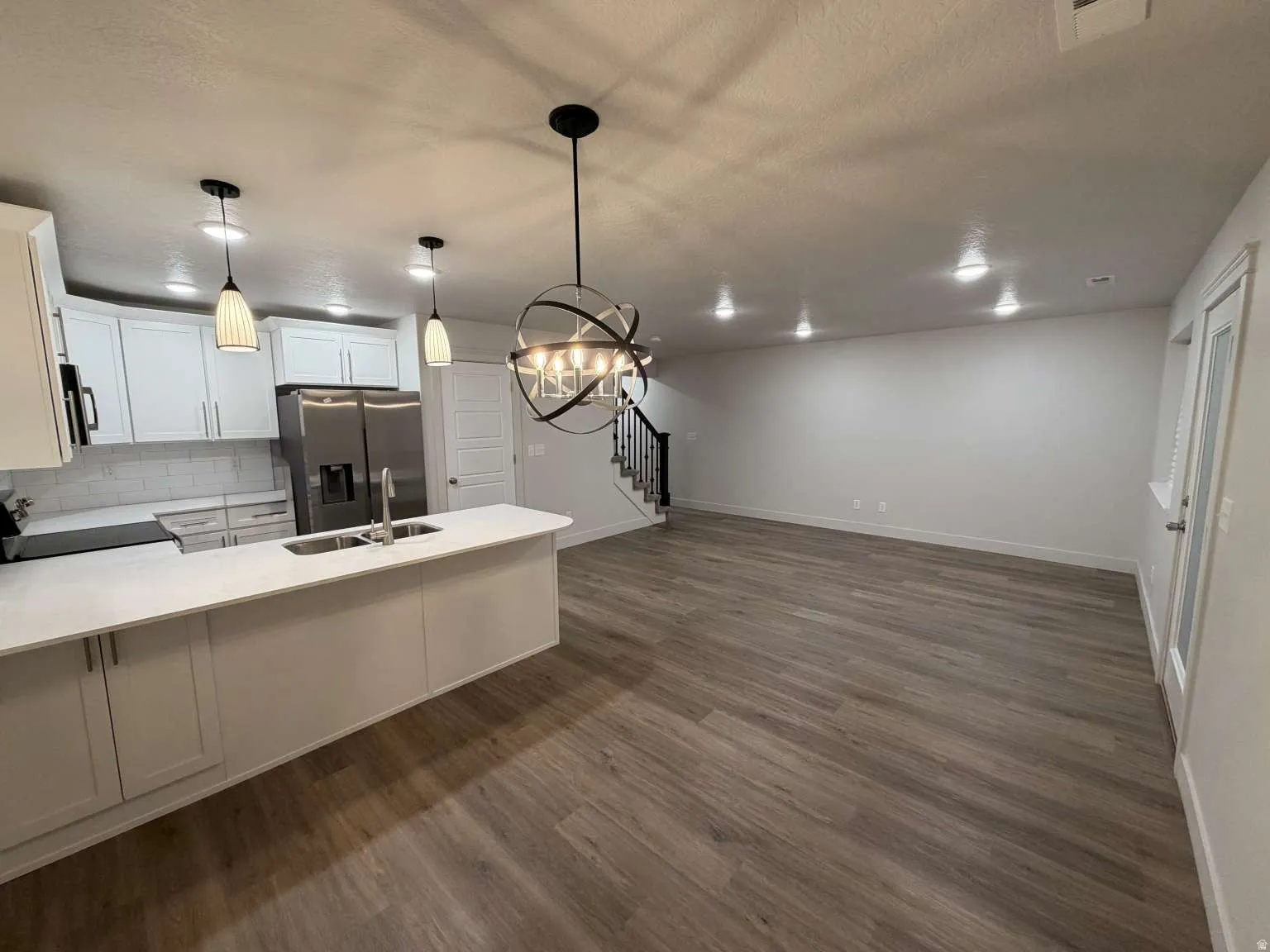 Open-concept living space featuring a kitchen with white cabinetry, stainless steel appliances, a white subway tile backsplash, and a large island with a double sink and pendant lighting