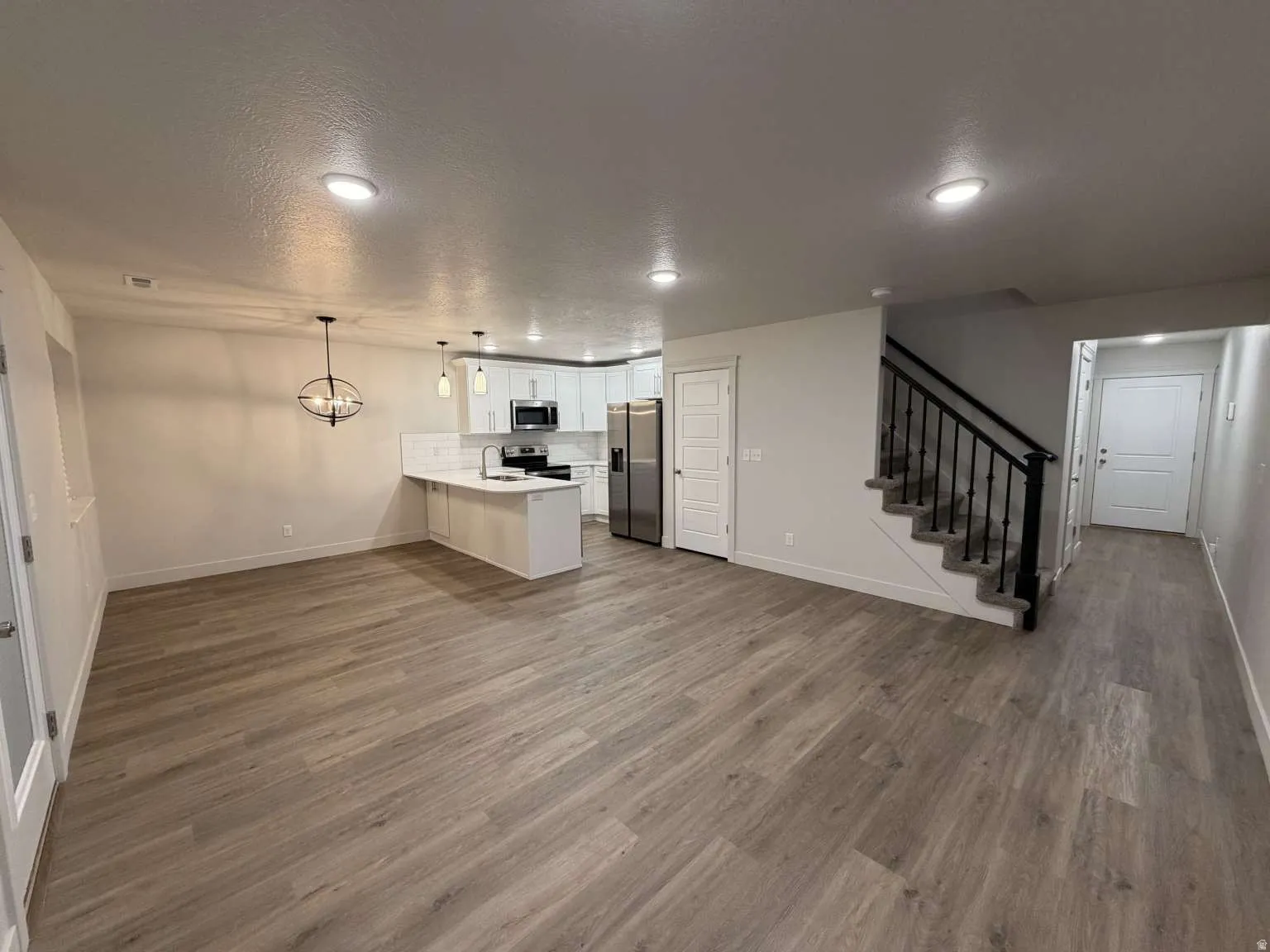 Combined living and kitchen area featuring wood-finish flooring, recessed lighting, and contemporary light fixtures
