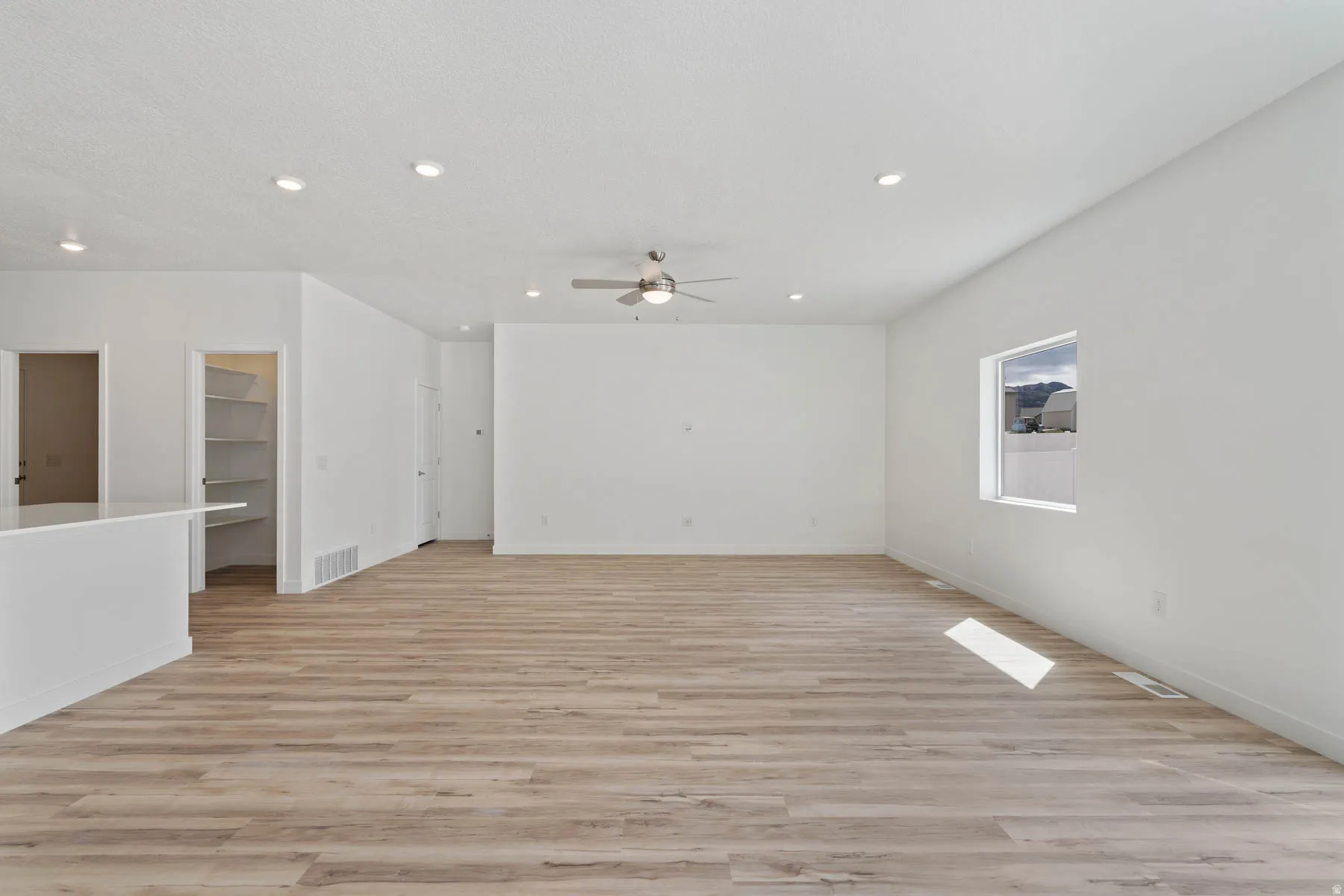 Expansive living area with wood-finish flooring, recessed lighting, and a ceiling fan