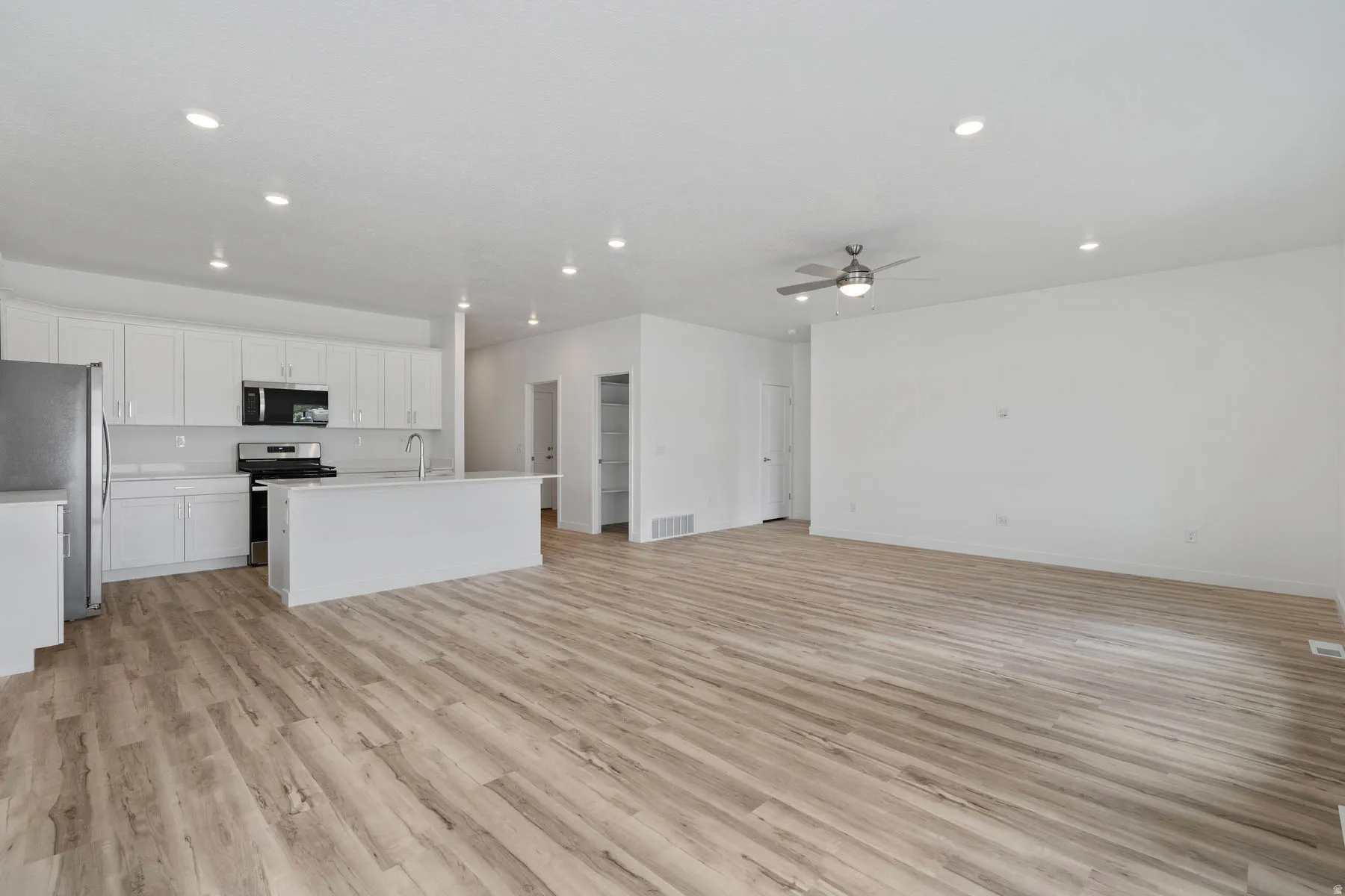 Contemporary open-concept living area featuring wood-finish flooring, recessed lighting, and a modern ceiling fan