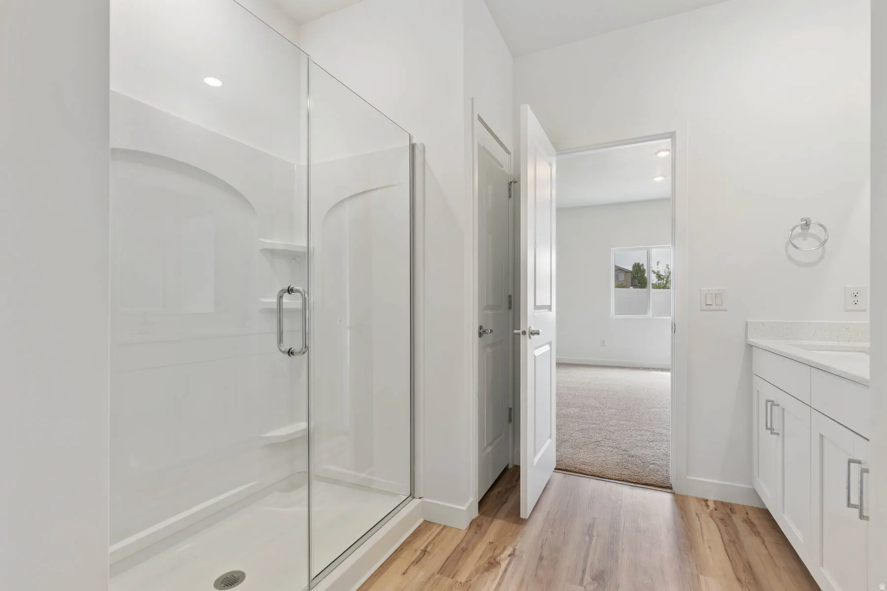 Glass-enclosed shower with integrated shelving, accompanied by a single-sink vanity with white cabinetry and a light-toned countertop