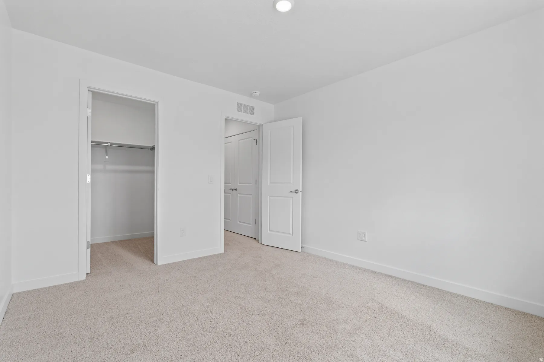 Room featuring neutral tone carpeting, white walls, a single ceiling light fixture, a closet with a metal hanging rod, and a white paneled door with a silver-tone handle
