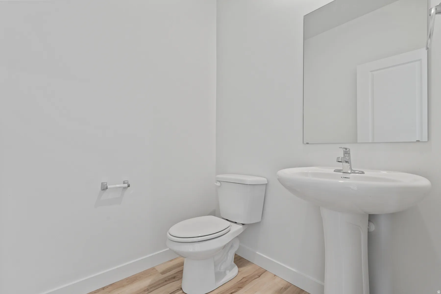 Pedestal sink with chrome faucet, wall-mounted mirror, and wood-finish flooring
