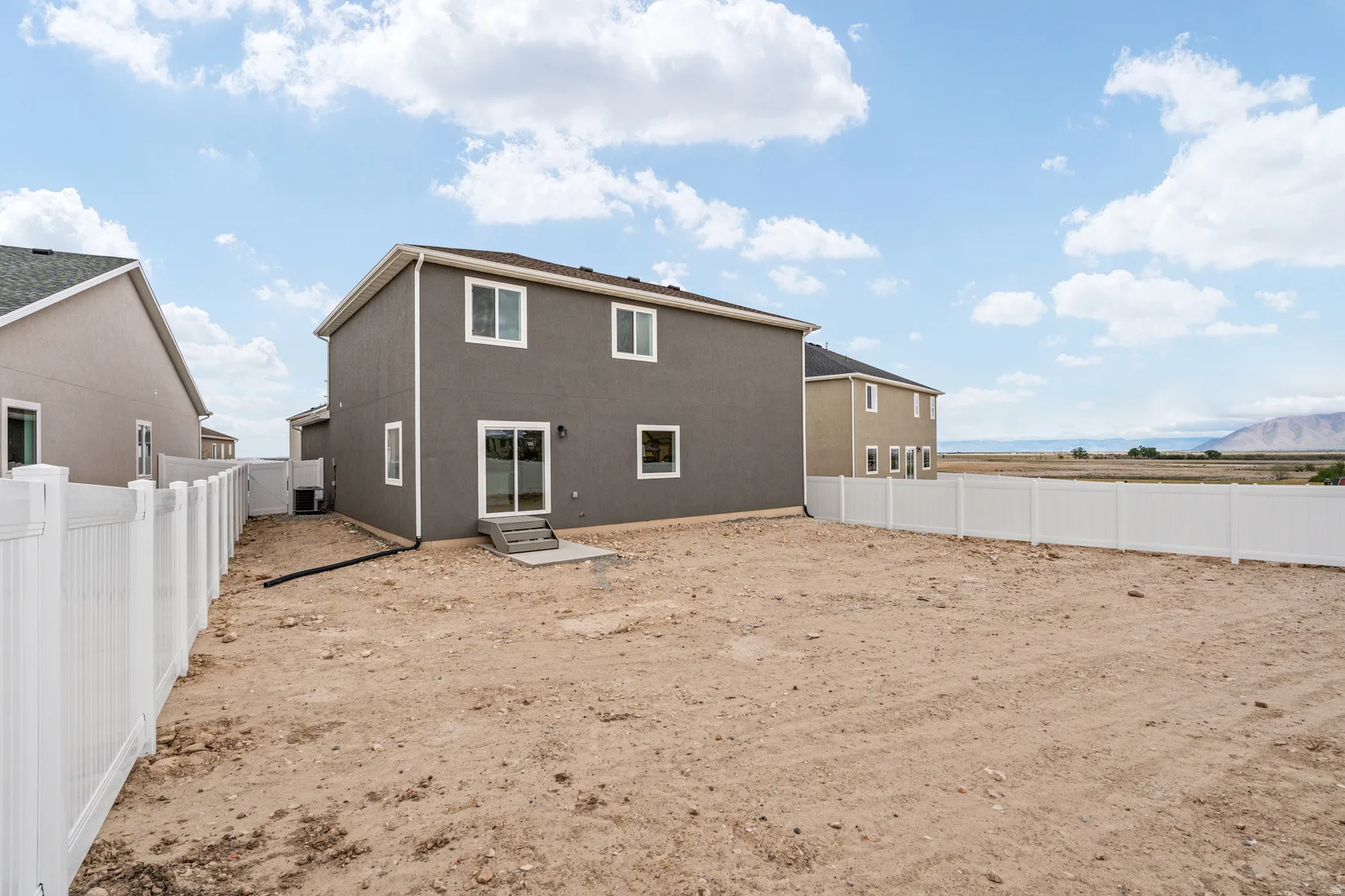 Expansive backyard featuring a newly installed white vinyl fence, a concrete patio, and a sliding glass door