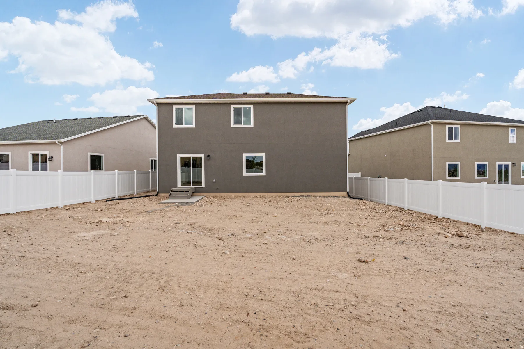 Expansive rear yard with privacy fencing and a two-story residence featuring a sliding glass door and windows