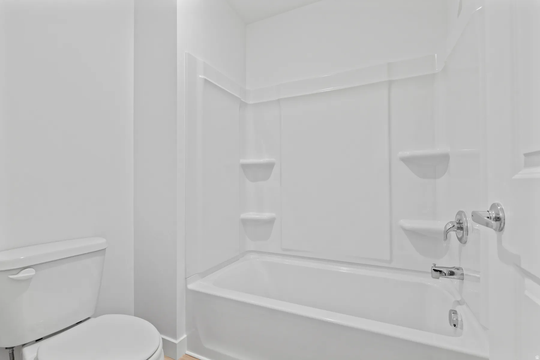 Tub and shower combination featuring a white surround, integrated shelving, and chrome fixtures