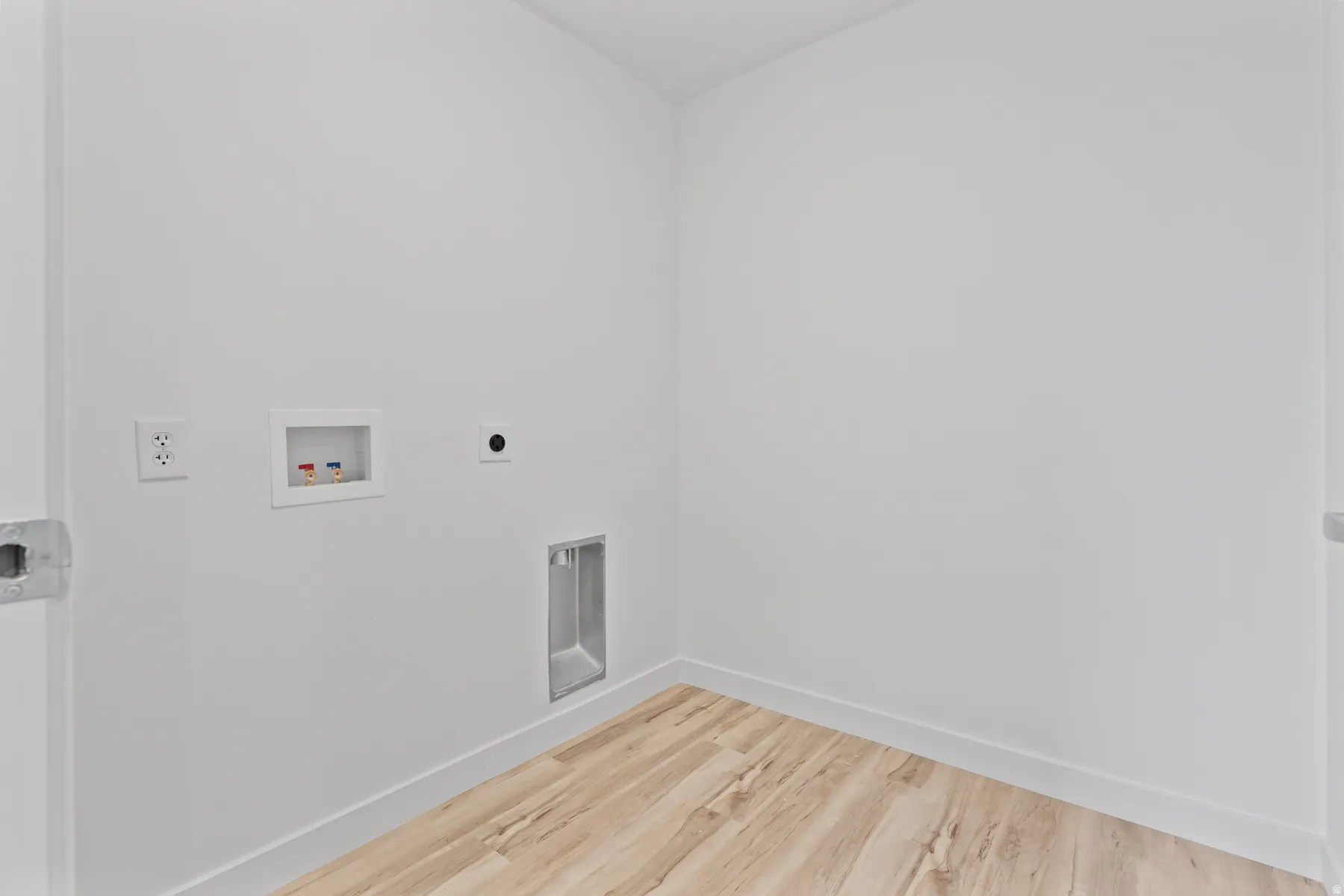Dedicated laundry area featuring a light wood-finish floor, white baseboards, and white walls
