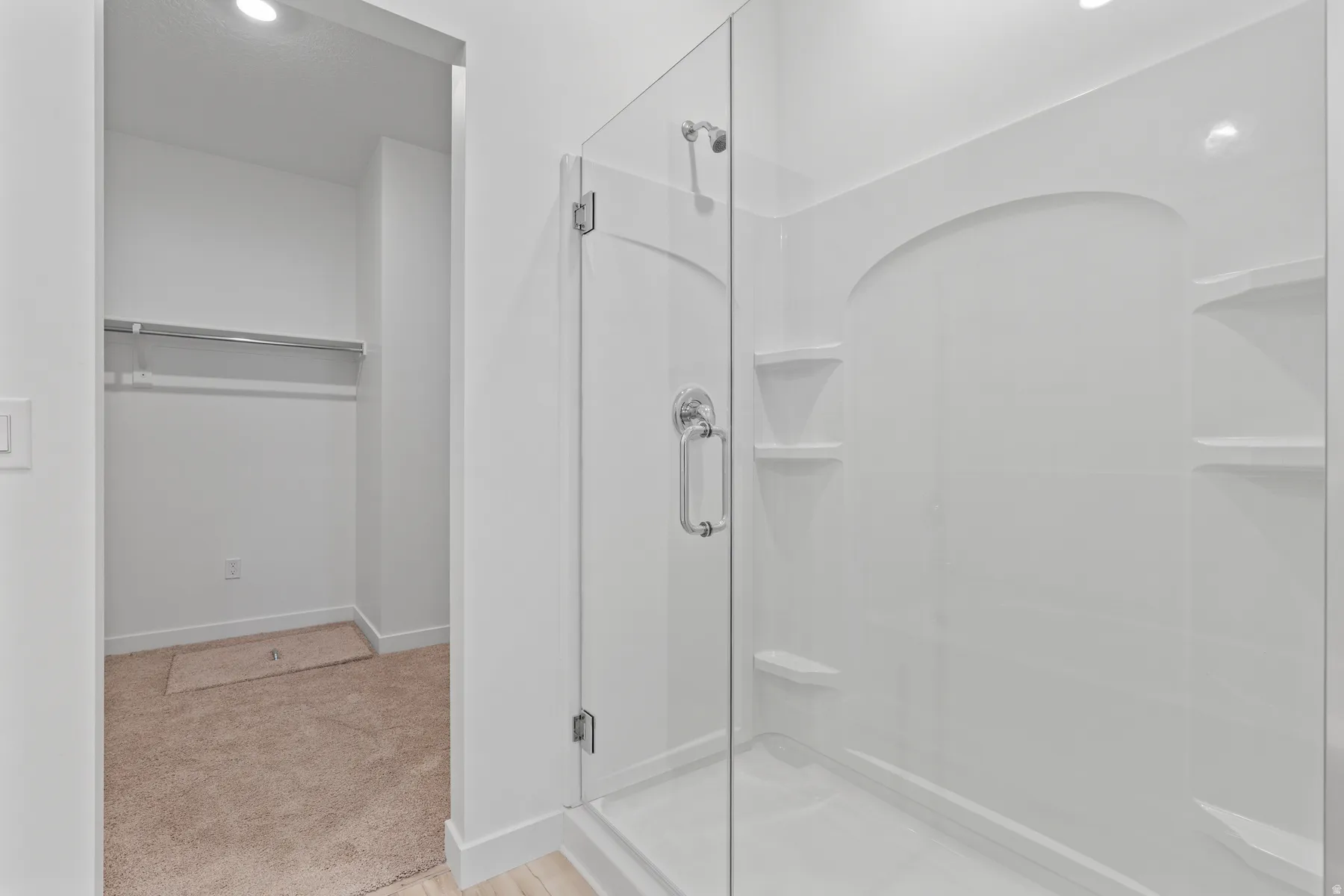 Shower enclosure featuring a clear glass door, chrome hardware, integrated shelving, and a white finish
