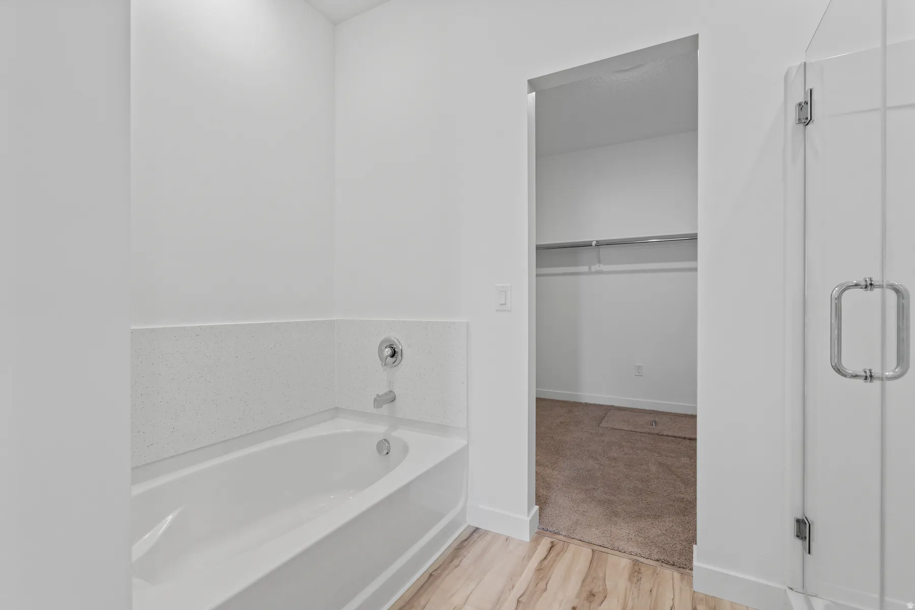 White soaking tub with chrome fixtures, surrounded by white walls and a light-toned wood-finish floor