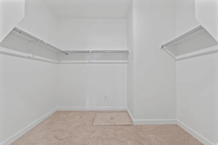 Spacious walk-in closet featuring light-colored carpet, white walls, white baseboards, and built-in metal shelving and hanging rods