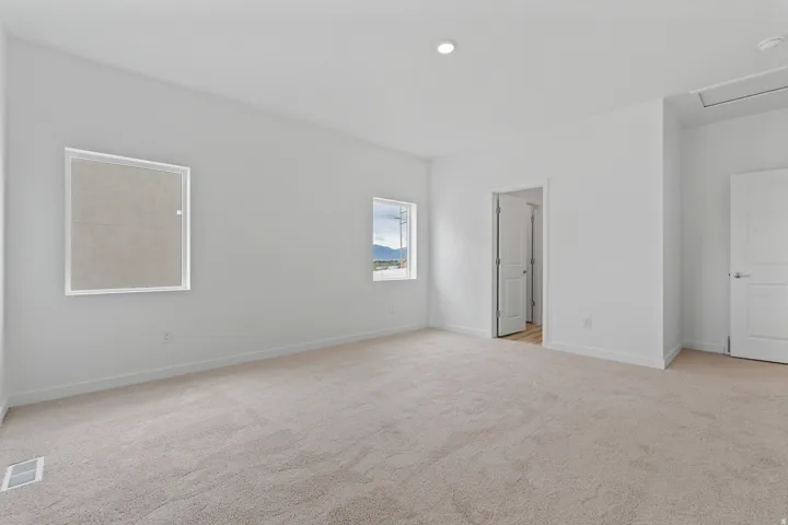 Spacious room featuring neutral carpeting, white painted walls, two windows, recessed lighting, and white baseboards