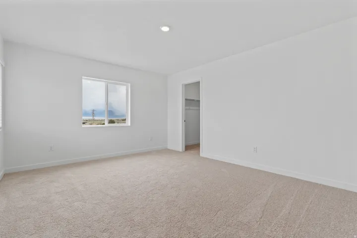 Carpeted interior space featuring a window with a white frame, recessed lighting, and a closet with shelving