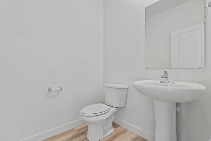 Pedestal sink with chrome faucet, wall-mounted mirror, and wood-finish flooring