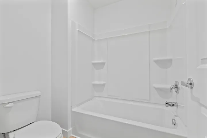 Tub and shower combination featuring a white surround, integrated shelving, and chrome fixtures
