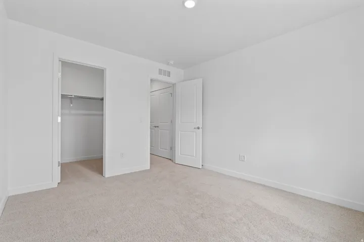 Room featuring neutral tone carpeting, white walls, a single ceiling light fixture, a closet with a metal hanging rod, and a white paneled door with a silver-tone handle